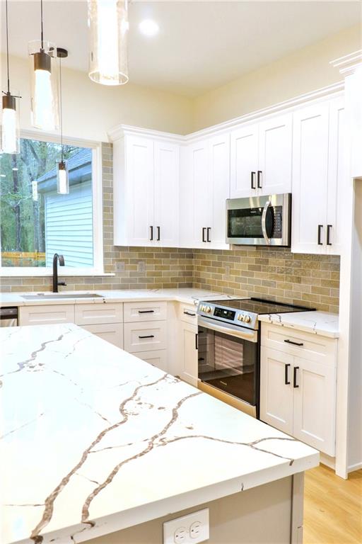 kitchen with pendant lighting, white cabinets, appliances with stainless steel finishes, decorative backsplash, and sink