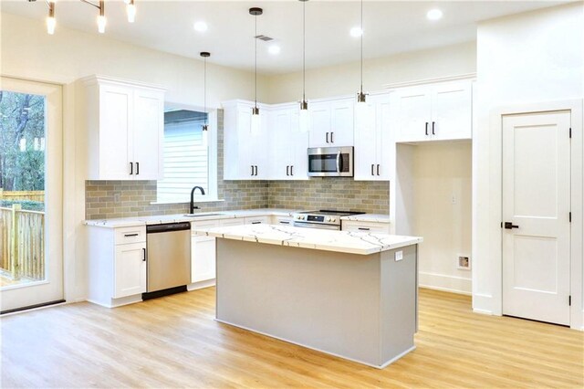 kitchen featuring decorative light fixtures, white cabinets, stainless steel appliances, and a kitchen island