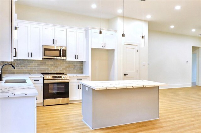 kitchen featuring white cabinets, appliances with stainless steel finishes, a center island, sink, and backsplash