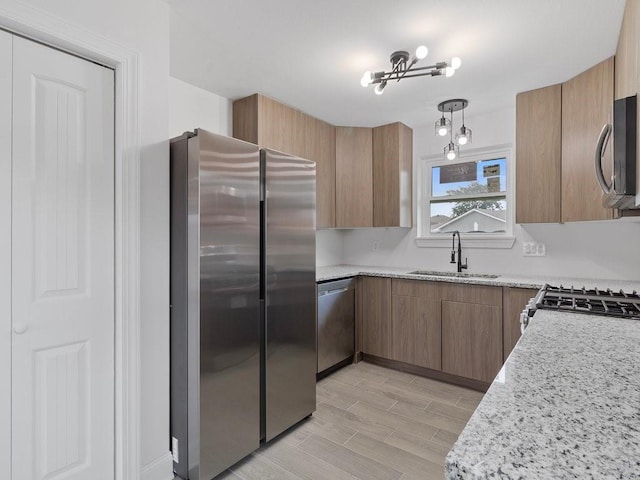 kitchen with appliances with stainless steel finishes, sink, light stone counters, and decorative light fixtures