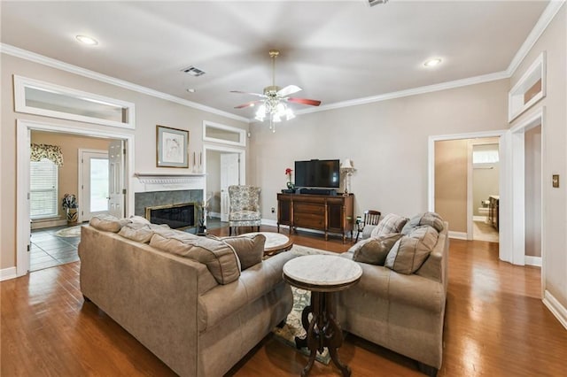 living room featuring hardwood / wood-style flooring, a premium fireplace, crown molding, and ceiling fan