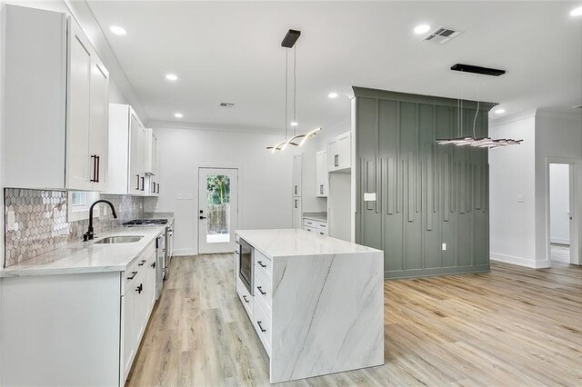 kitchen featuring sink, white cabinetry, a center island, pendant lighting, and light stone countertops