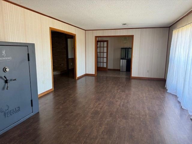 unfurnished living room featuring dark wood-type flooring, a textured ceiling, and crown molding