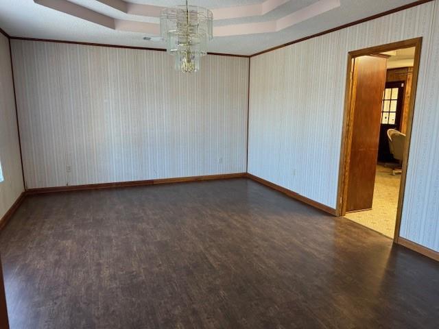 empty room featuring a raised ceiling, dark wood-type flooring, crown molding, and a chandelier