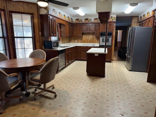 kitchen featuring a kitchen island, sink, wooden walls, dark brown cabinetry, and stainless steel appliances