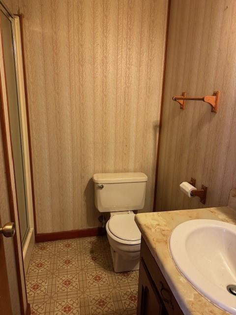 bathroom with a shower with door, toilet, vanity, and wooden walls