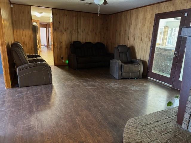 living room featuring dark wood-type flooring, ceiling fan, and wood walls