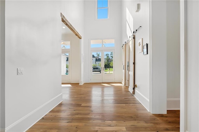 foyer with a towering ceiling, a barn door, hardwood / wood-style flooring, and french doors