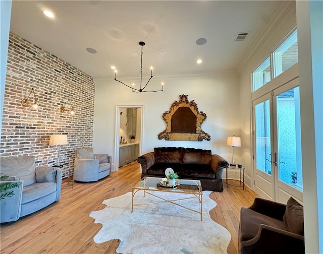 living room with brick wall, french doors, ornamental molding, a notable chandelier, and light wood-type flooring