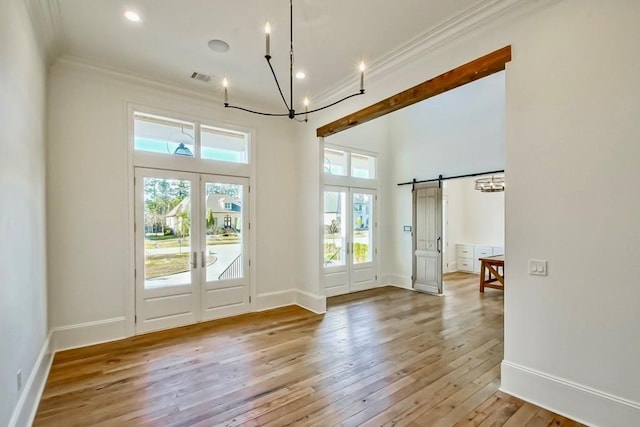 entryway with a barn door, french doors, crown molding, and light hardwood / wood-style floors