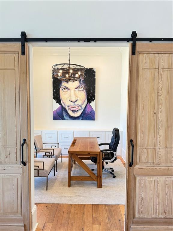 office space with a chandelier, a barn door, and light wood-type flooring