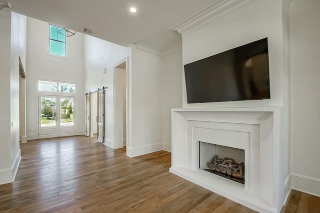 unfurnished living room with french doors, ornamental molding, a barn door, and hardwood / wood-style flooring