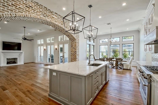 kitchen with appliances with stainless steel finishes, a kitchen island with sink, pendant lighting, light stone counters, and sink