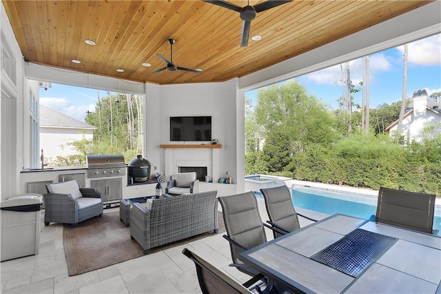 view of patio with ceiling fan, area for grilling, an outdoor living space with a fireplace, and exterior kitchen