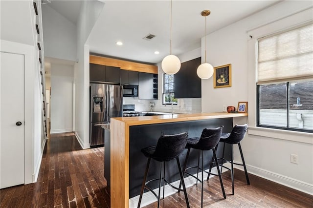 kitchen featuring backsplash, kitchen peninsula, hanging light fixtures, stainless steel fridge with ice dispenser, and a kitchen breakfast bar