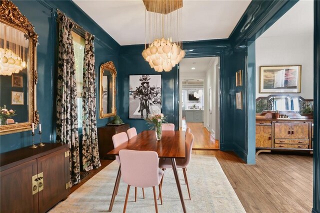 dining space with hardwood / wood-style flooring, crown molding, and an inviting chandelier