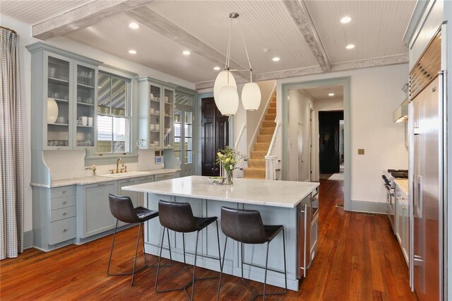 kitchen with a breakfast bar area, beamed ceiling, dark wood-type flooring, pendant lighting, and a center island