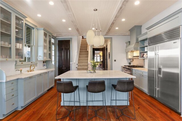 kitchen featuring custom exhaust hood, a center island, decorative light fixtures, high quality appliances, and sink