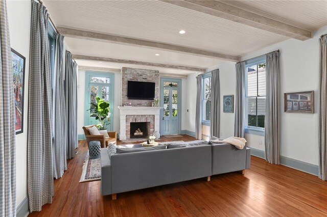 living room featuring a brick fireplace, wood-type flooring, and beamed ceiling