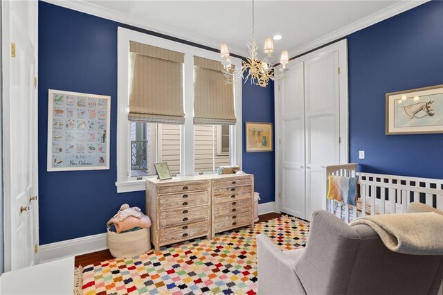 bedroom featuring a nursery area, a closet, wood-type flooring, a chandelier, and crown molding