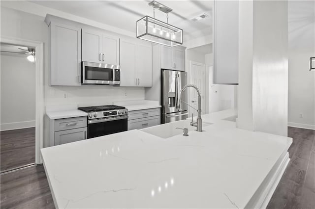 kitchen with dark hardwood / wood-style floors, gray cabinetry, hanging light fixtures, light stone counters, and stainless steel appliances