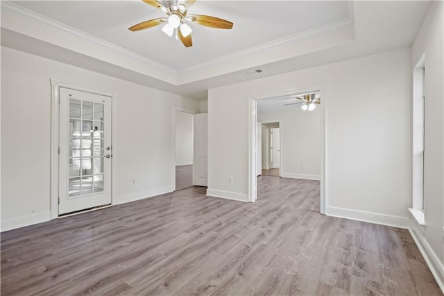 empty room with ceiling fan, a tray ceiling, and light hardwood / wood-style flooring