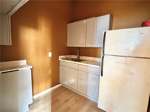 kitchen with light hardwood / wood-style floors, sink, white cabinets, and white fridge