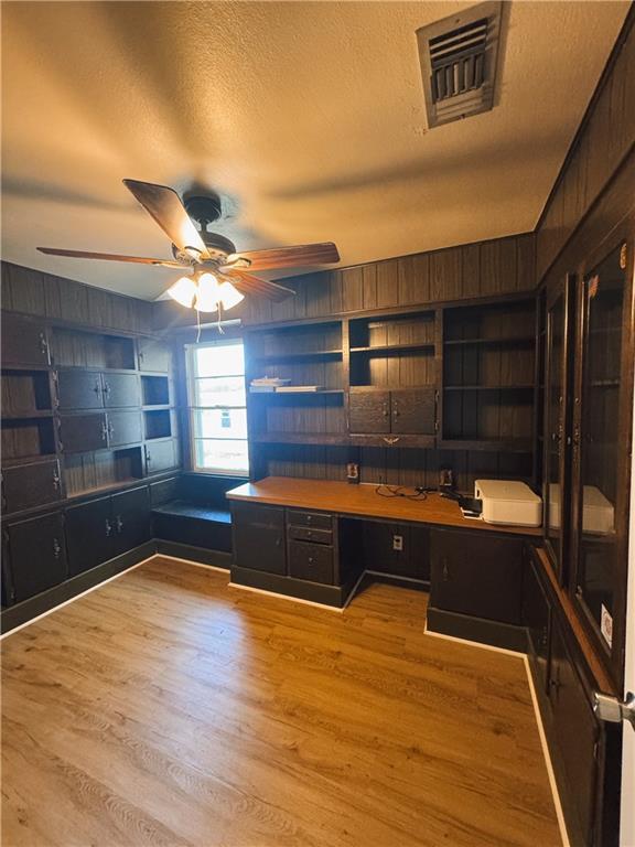 unfurnished office featuring built in desk, built in shelves, ceiling fan, and light hardwood / wood-style flooring