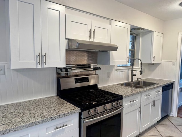 kitchen with sink, white cabinetry, stainless steel appliances, light tile patterned floors, and light stone counters