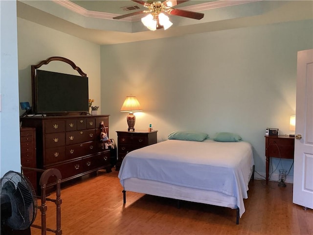 bedroom featuring ceiling fan, hardwood / wood-style flooring, a tray ceiling, and ornamental molding