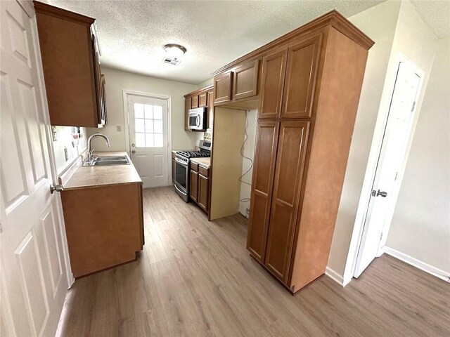 kitchen with light wood-type flooring, stainless steel appliances, a textured ceiling, and sink