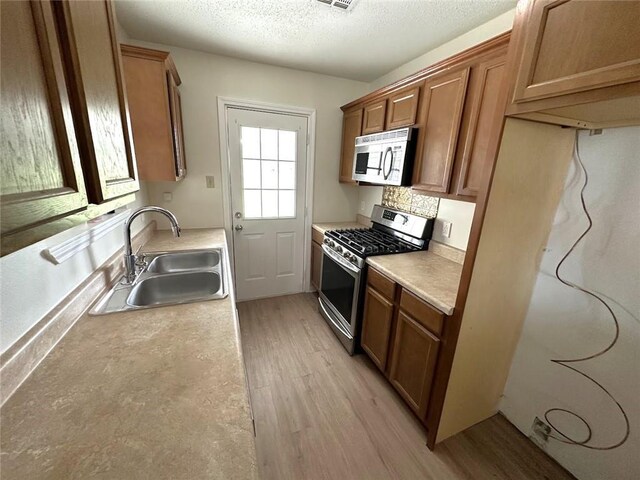 kitchen with sink, a textured ceiling, appliances with stainless steel finishes, and light hardwood / wood-style flooring