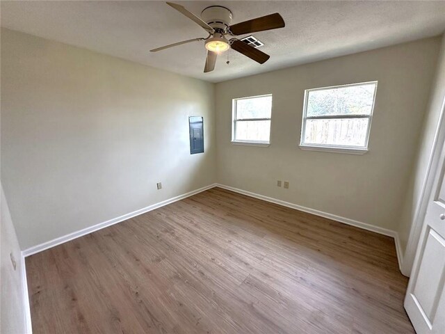 empty room with light wood-type flooring, ceiling fan, and electric panel