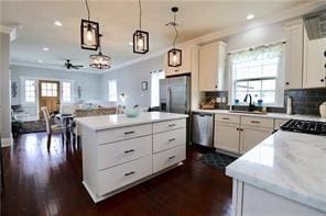 kitchen featuring appliances with stainless steel finishes, hanging light fixtures, white cabinets, a kitchen island, and ornamental molding