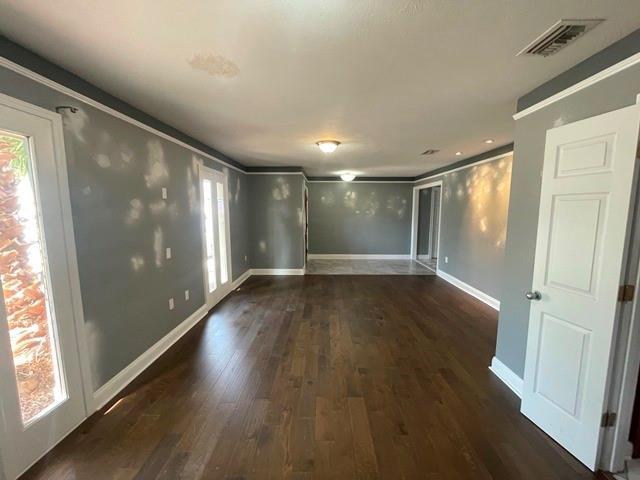 unfurnished room with baseboards, visible vents, dark wood finished floors, and crown molding