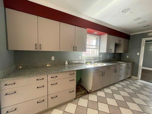 kitchen with stovetop, light stone countertops, crown molding, white cabinets, and sink