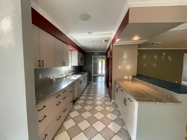 kitchen with crown molding, light floors, light stone counters, and white cabinets