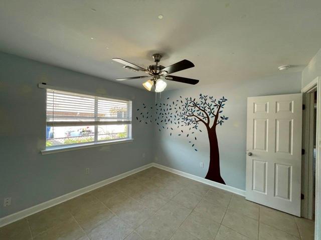 empty room with light tile patterned floors, a ceiling fan, and baseboards