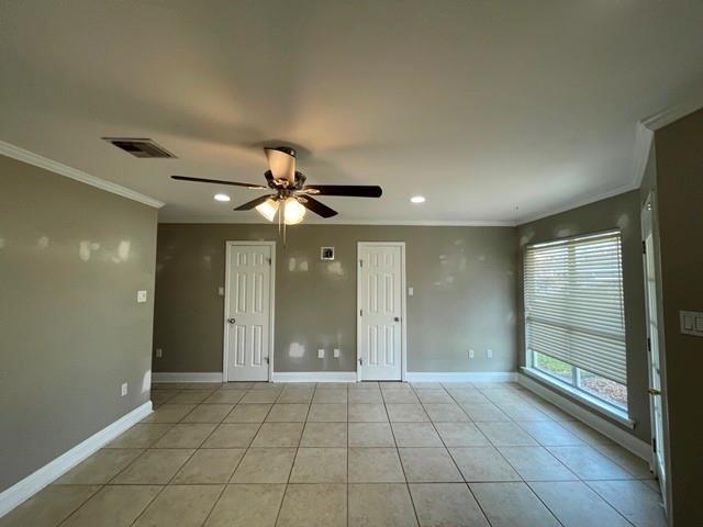 spare room featuring light tile patterned floors, baseboards, visible vents, a ceiling fan, and crown molding