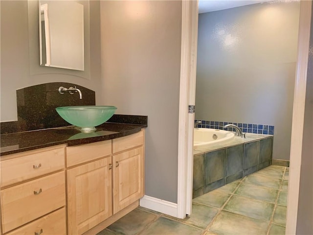 bathroom featuring tiled bath, baseboards, tile patterned flooring, and vanity