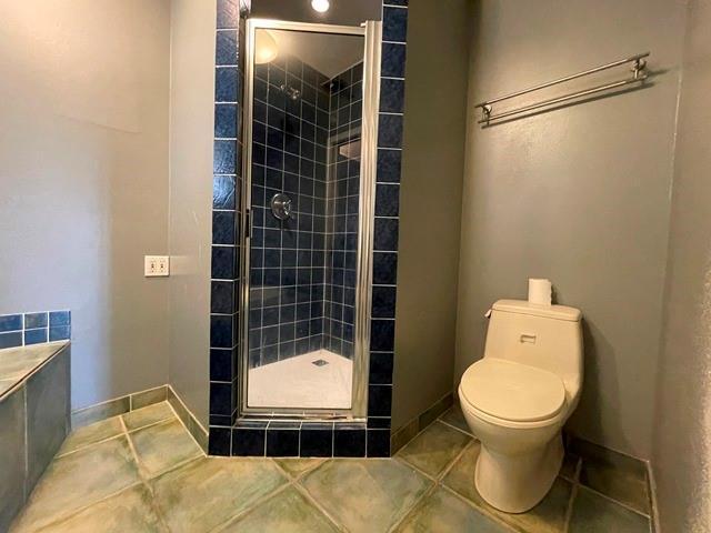 bathroom with baseboards, a shower stall, toilet, and tile patterned floors