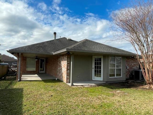 rear view of property with central AC, brick siding, roof with shingles, a lawn, and a patio area