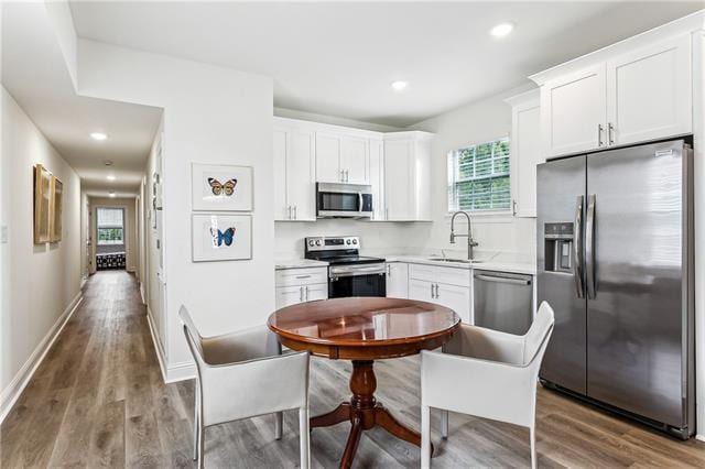 kitchen featuring white cabinets, wood finished floors, light countertops, stainless steel appliances, and a sink