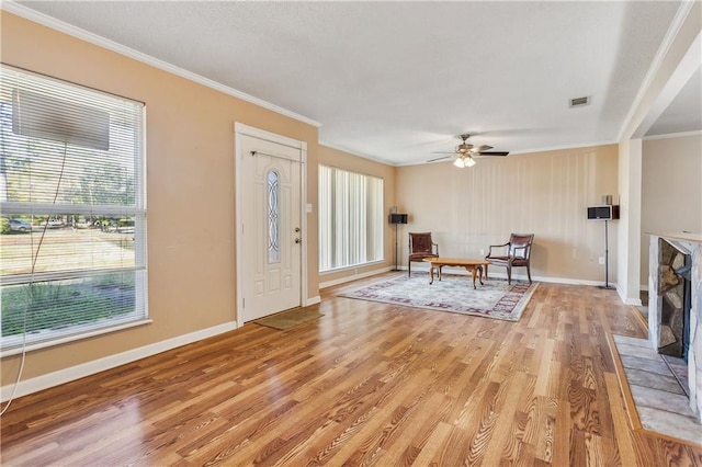 foyer entrance with ceiling fan, a tiled fireplace, crown molding, and hardwood / wood-style flooring