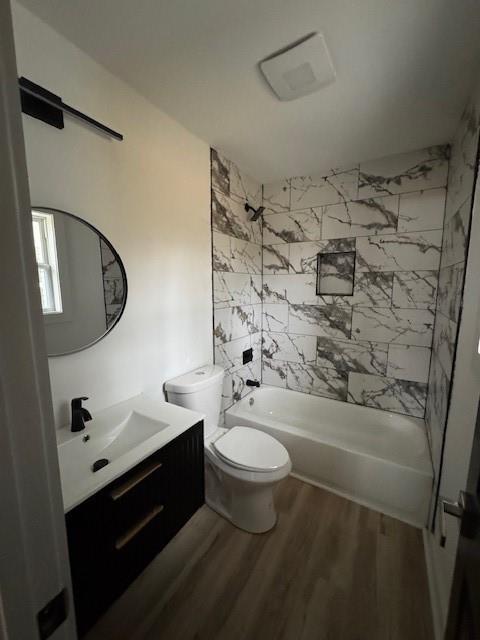 full bathroom with hardwood / wood-style flooring, tiled shower / bath, vanity, and toilet