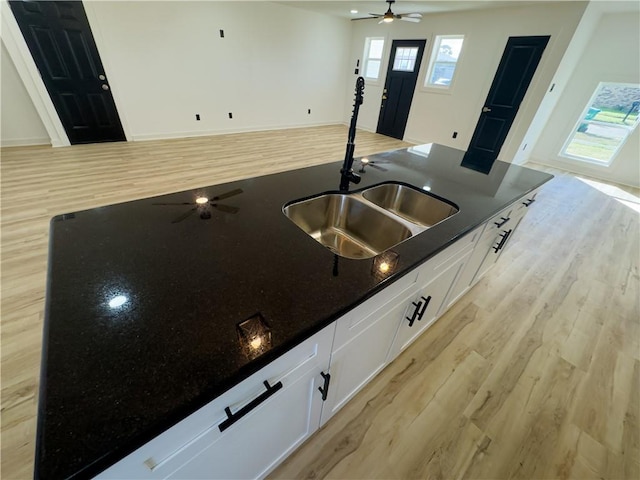 kitchen with dark stone counters, sink, light hardwood / wood-style flooring, and white cabinets