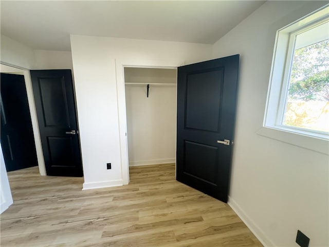 unfurnished bedroom featuring multiple windows, a closet, and light wood-type flooring