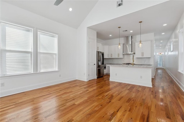 kitchen with stainless steel refrigerator with ice dispenser, wall chimney exhaust hood, decorative light fixtures, a kitchen island, and white cabinets