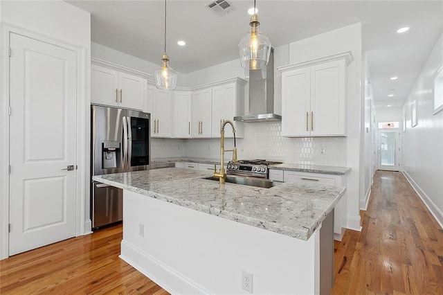 kitchen with white cabinets, a center island with sink, stainless steel fridge, and wall chimney exhaust hood