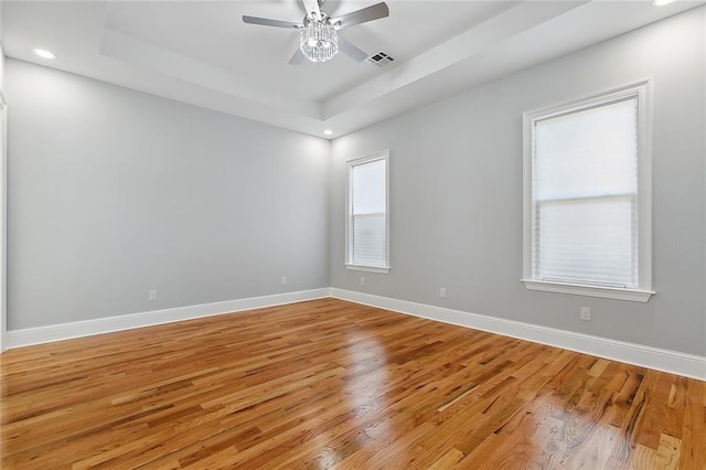 unfurnished room with light hardwood / wood-style floors, a raised ceiling, and ceiling fan